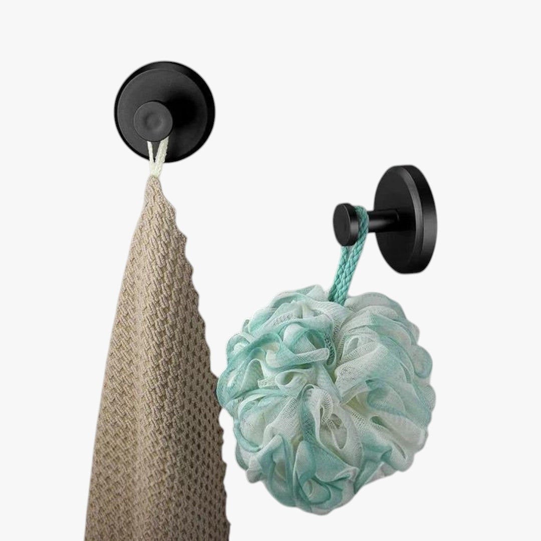 Roselva matte black suction hooks holding a beige towel and a teal loofah on a wall