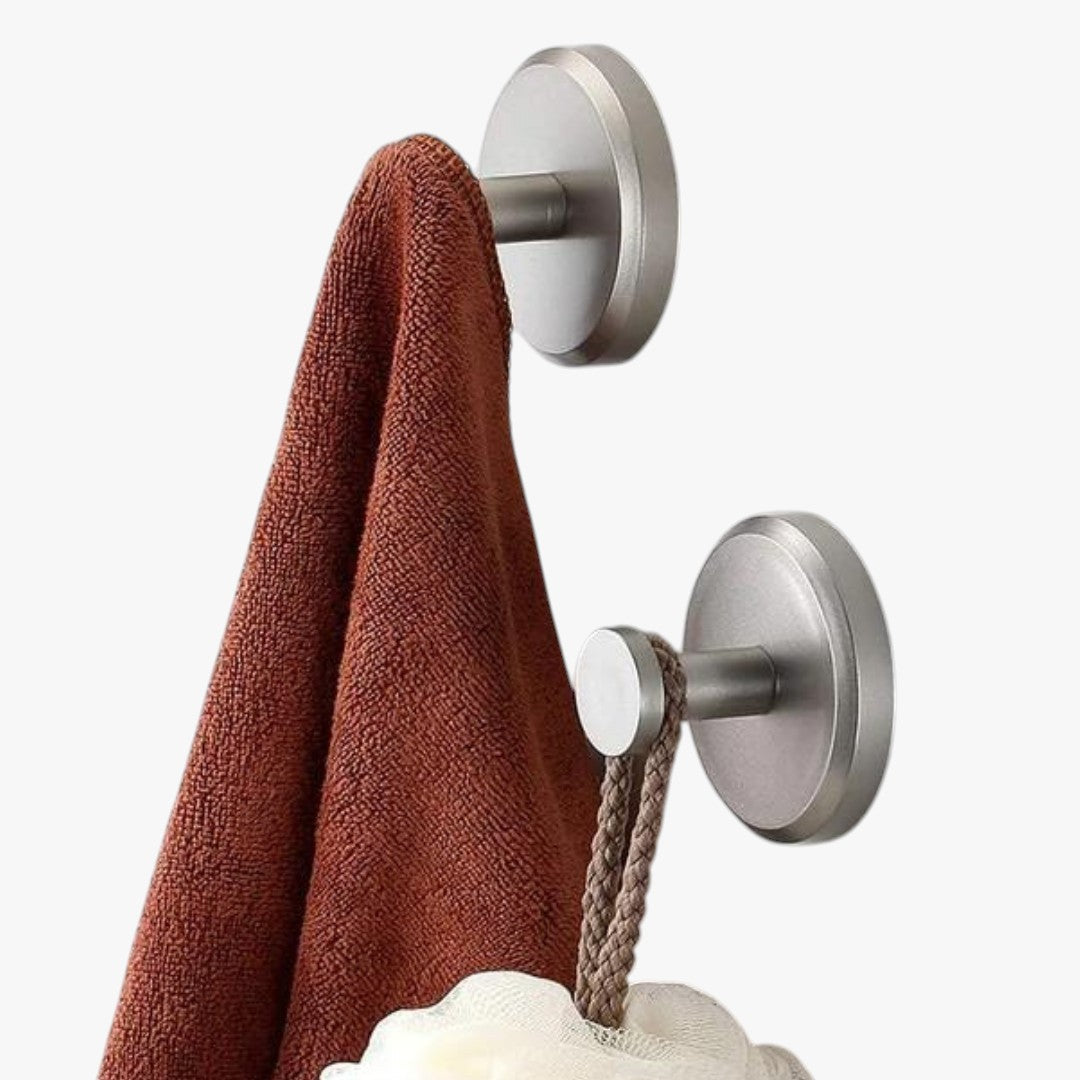 Roselva silver metal suction hooks holding a brown towel and a loofah on a smooth wall surface